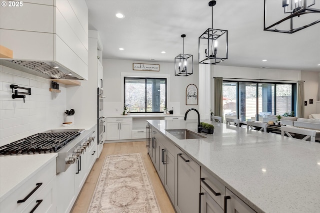 kitchen featuring appliances with stainless steel finishes, light stone counters, sink, white cabinetry, and decorative light fixtures