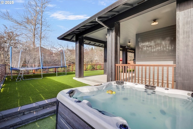 exterior space featuring a lawn, a hot tub, and a trampoline