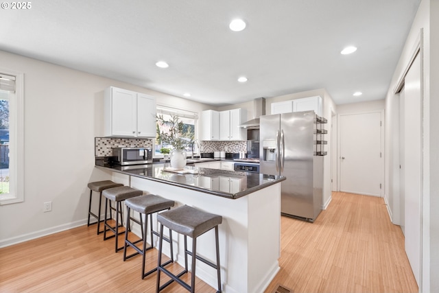 kitchen with wall chimney exhaust hood, sink, white cabinetry, appliances with stainless steel finishes, and kitchen peninsula