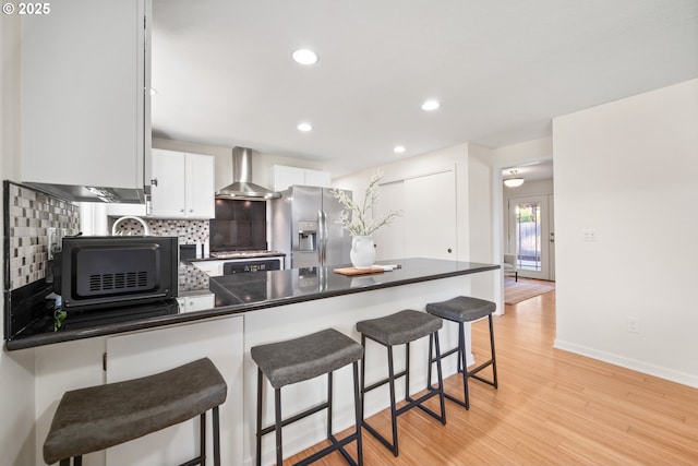 kitchen featuring white cabinetry, kitchen peninsula, stainless steel refrigerator with ice dispenser, wall chimney range hood, and light wood-type flooring