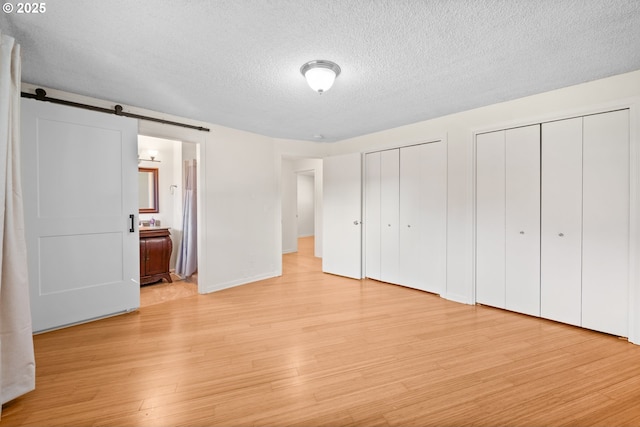 unfurnished bedroom featuring connected bathroom, a textured ceiling, light wood-type flooring, two closets, and a barn door