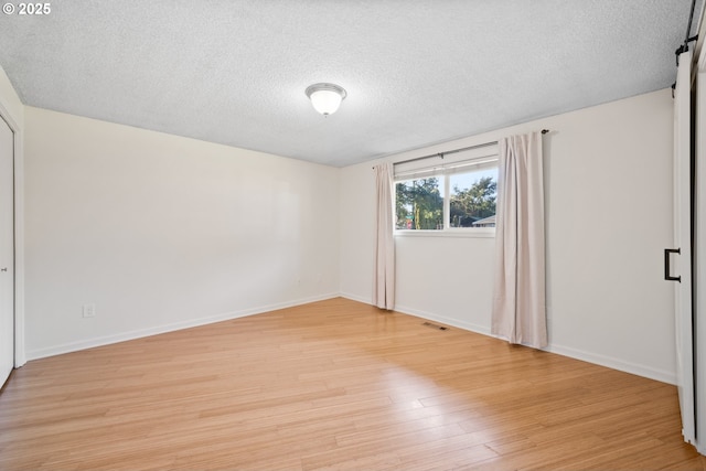 empty room featuring a barn door, light hardwood / wood-style floors, and a textured ceiling