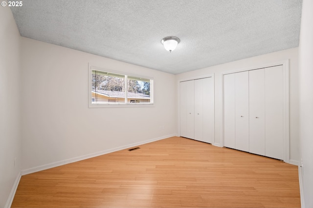 unfurnished bedroom with two closets, a textured ceiling, and light wood-type flooring