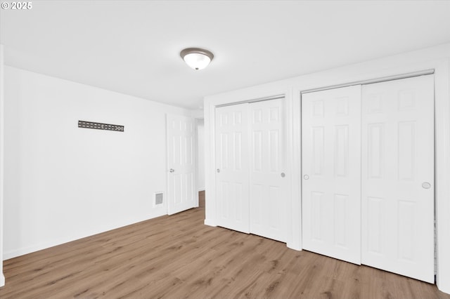 unfurnished bedroom featuring multiple closets and light wood-type flooring