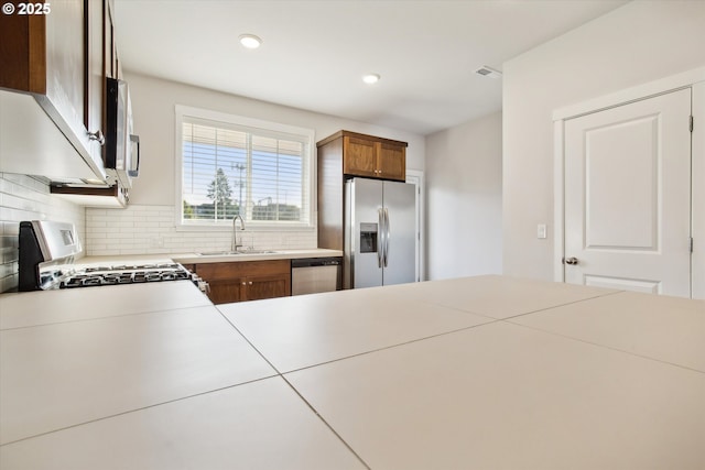 kitchen with tasteful backsplash, light countertops, appliances with stainless steel finishes, brown cabinetry, and a sink