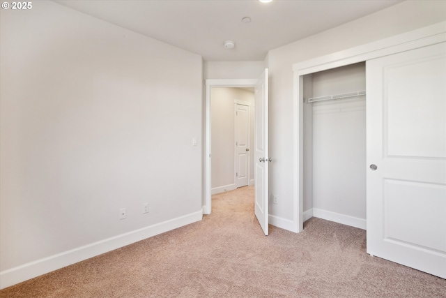unfurnished bedroom featuring a closet, light colored carpet, and baseboards