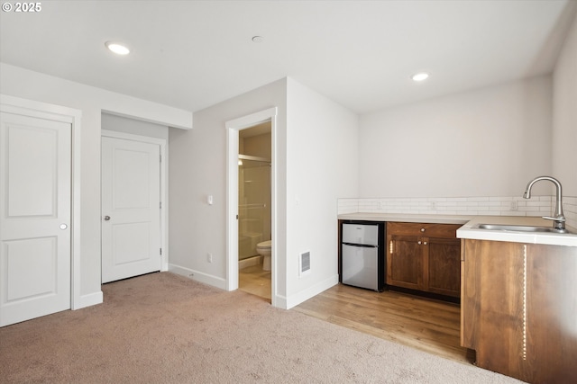 kitchen with baseboards, freestanding refrigerator, a sink, light countertops, and light carpet