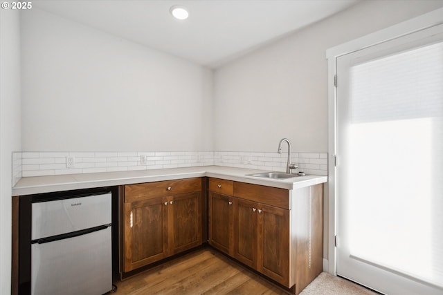 kitchen with a sink, light countertops, fridge, tasteful backsplash, and light wood-type flooring