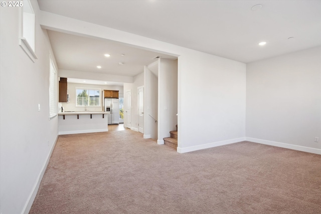 unfurnished living room with recessed lighting, light colored carpet, stairs, and baseboards