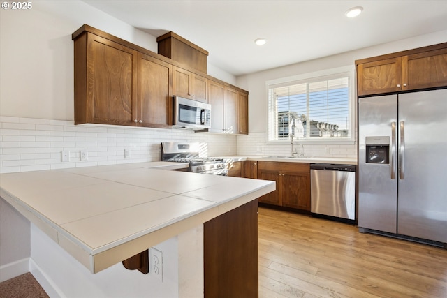 kitchen featuring tasteful backsplash, light wood-style flooring, a peninsula, stainless steel appliances, and a sink