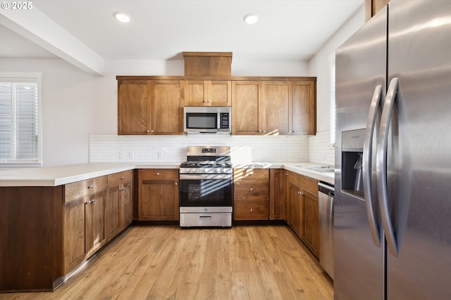 13020 SW Larkwood Pl, Sherwood, OR 97140 - kitchen with stainless steel appliances, a peninsula, tasteful backsplash, light countertops, and light wood-style floors