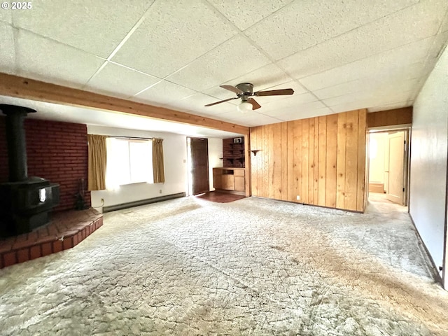 524 Buckhorn Rd, Roseburg, OR 97470 - unfurnished living room featuring wooden walls, a baseboard radiator, ceiling fan, a drop ceiling, and a wood stove