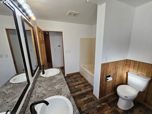 bathroom featuring toilet, wooden walls, visible vents, and a sink