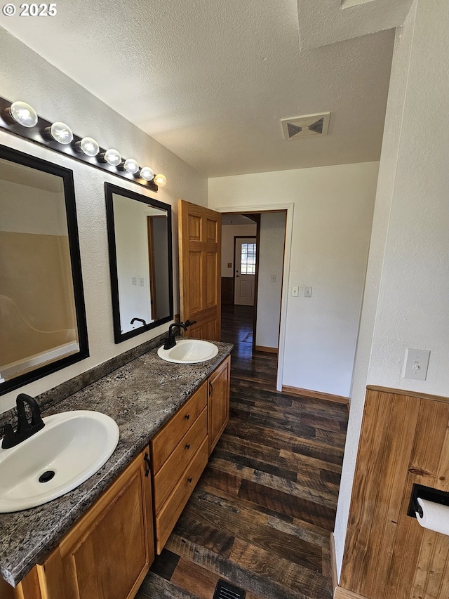 bathroom with double vanity, a sink, a textured ceiling, and wood finished floors