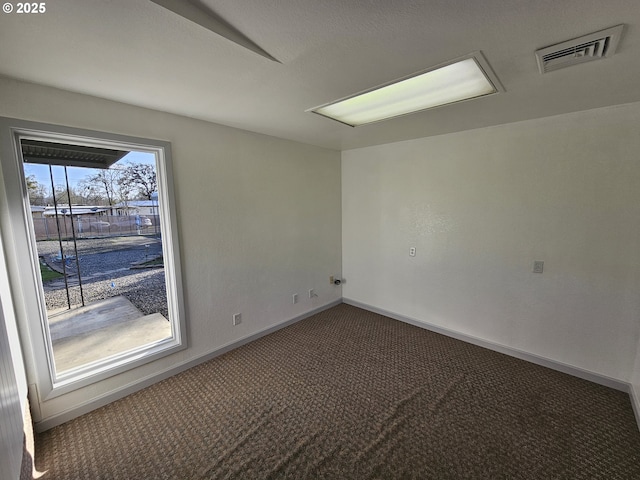 spare room with dark carpet, visible vents, and baseboards