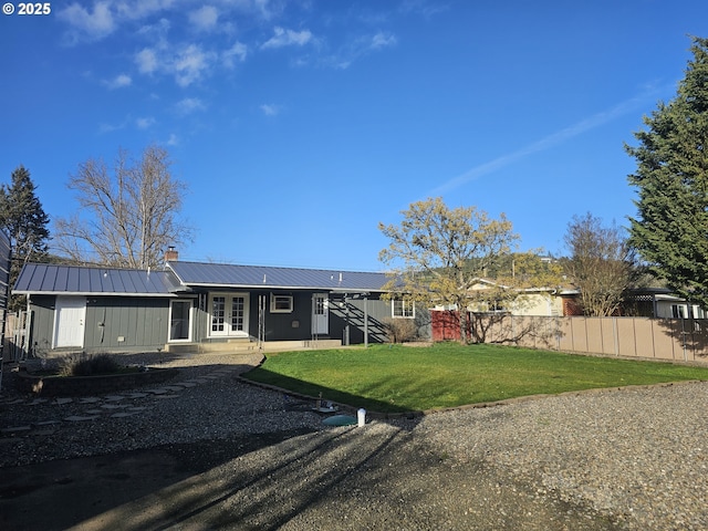 back of house with metal roof, a lawn, a chimney, and fence