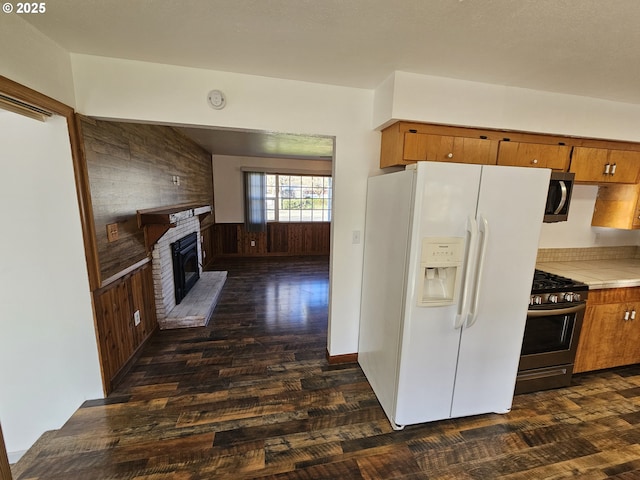 kitchen with appliances with stainless steel finishes, a brick fireplace, light countertops, and dark wood finished floors