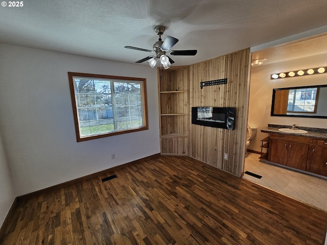 interior space featuring dark wood finished floors, visible vents, wood walls, a textured ceiling, and a sink