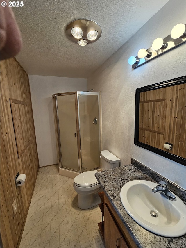 bathroom featuring a textured ceiling, toilet, vanity, a shower stall, and tile patterned floors