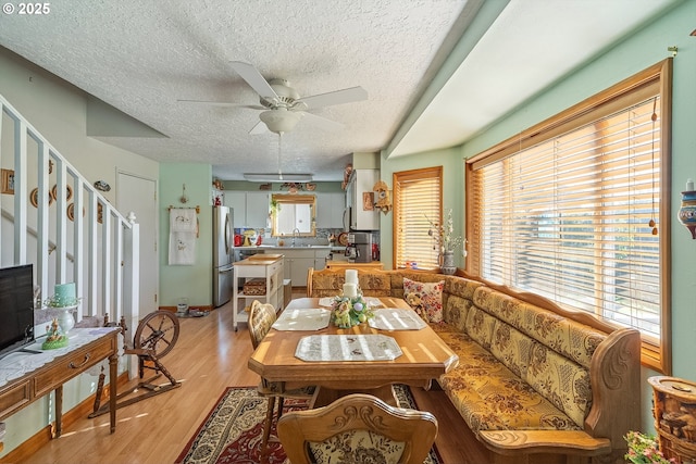 dining space with a ceiling fan, a textured ceiling, light wood-style floors, and a healthy amount of sunlight