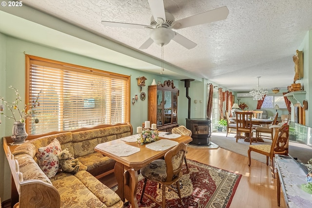 living room with wood finished floors, a wood stove, an AC wall unit, a textured ceiling, and ceiling fan with notable chandelier