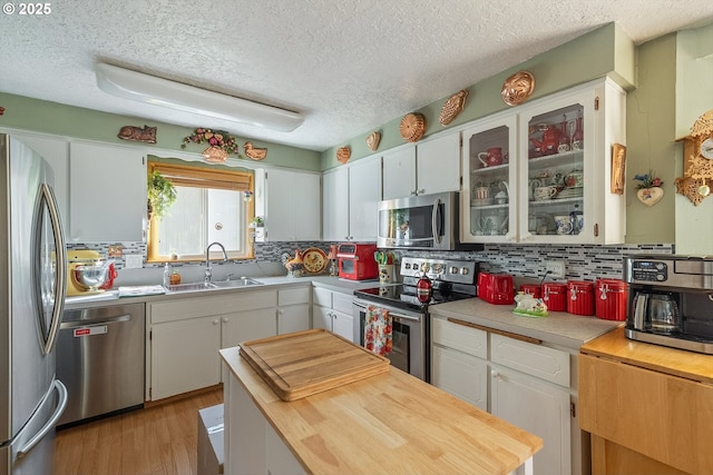 kitchen with stainless steel appliances, a sink, decorative backsplash, a textured ceiling, and white cabinetry