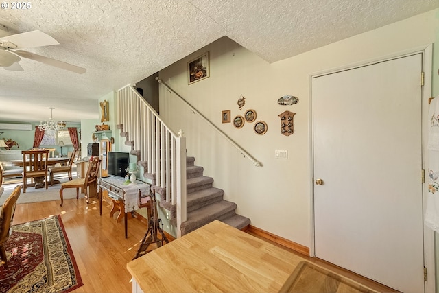 stairway with ceiling fan, wood finished floors, a textured ceiling, and a wall unit AC