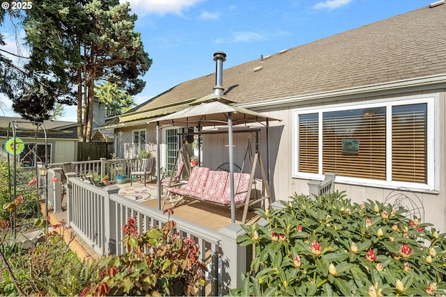 rear view of property featuring a wooden deck, a gazebo, fence, and a shingled roof