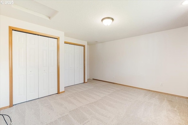 unfurnished bedroom with light colored carpet, attic access, baseboards, and two closets