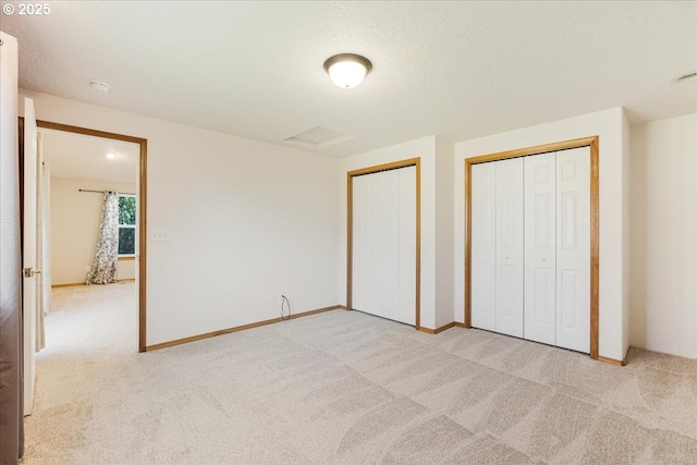 unfurnished bedroom with baseboards, light carpet, and two closets