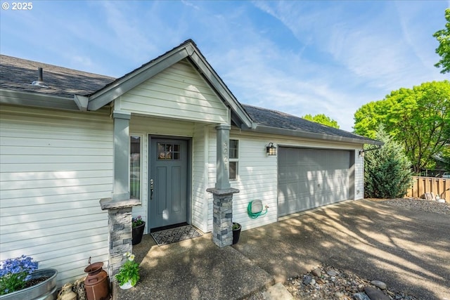 entrance to property with an attached garage, a shingled roof, aphalt driveway, and fence