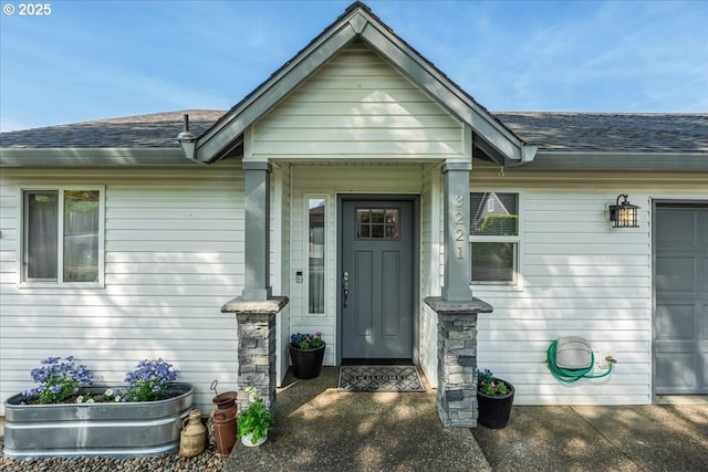 view of exterior entry with an attached garage and a shingled roof