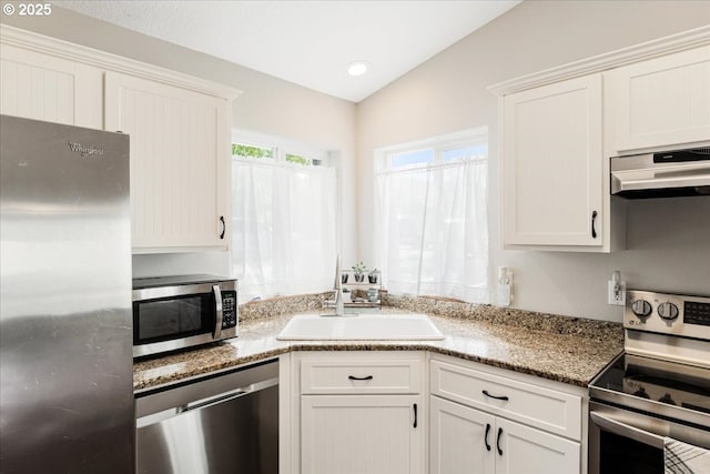 kitchen with white cabinets, light stone countertops, a sink, stainless steel appliances, and under cabinet range hood