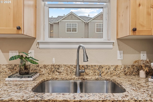 details featuring light stone countertops, a textured wall, a sink, and light brown cabinetry