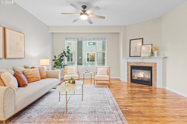 living area featuring ceiling fan, a fireplace, baseboards, and wood finished floors