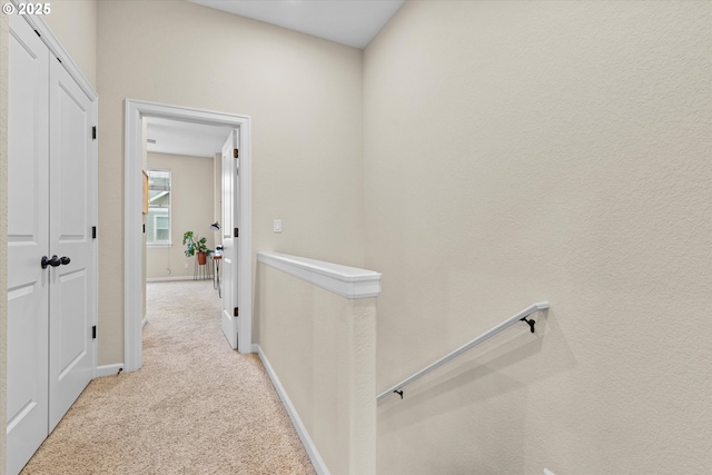 corridor with baseboards, an upstairs landing, and light colored carpet