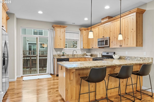 kitchen featuring light stone counters, decorative light fixtures, appliances with stainless steel finishes, light wood-type flooring, and a peninsula