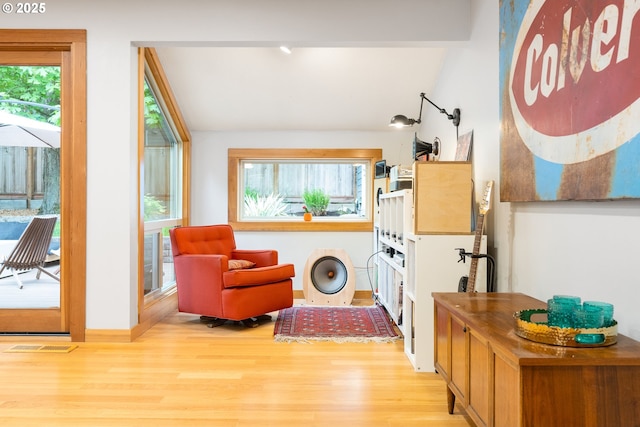 living area featuring a healthy amount of sunlight, vaulted ceiling, wood finished floors, and visible vents