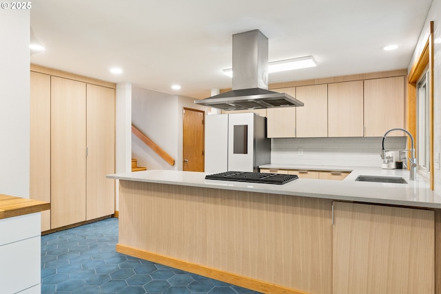kitchen with island range hood, refrigerator, black gas cooktop, a sink, and a peninsula
