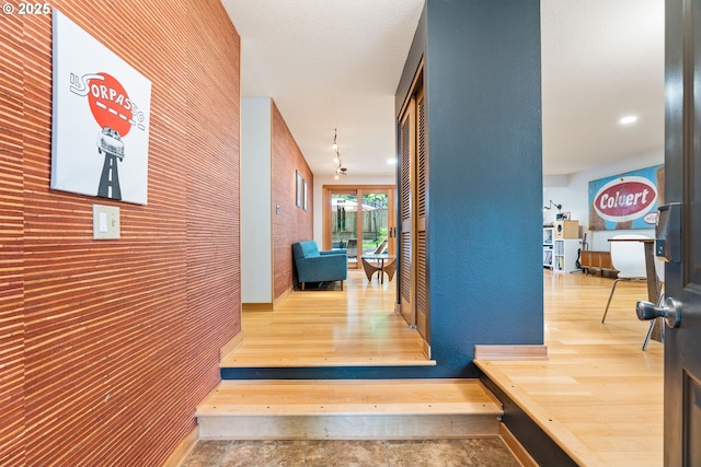 hallway featuring an accent wall, wood walls, and wood finished floors