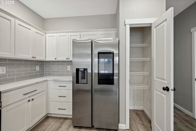 kitchen with light wood finished floors, light stone counters, decorative backsplash, stainless steel refrigerator with ice dispenser, and white cabinets