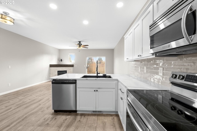 kitchen with light wood finished floors, a peninsula, a sink, stainless steel appliances, and tasteful backsplash