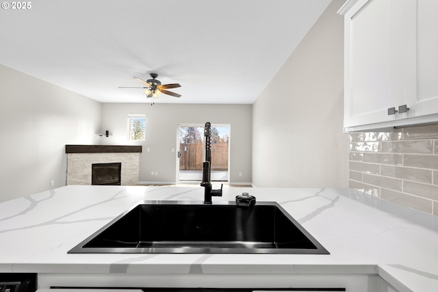 kitchen featuring light stone counters, a fireplace, open floor plan, and a sink