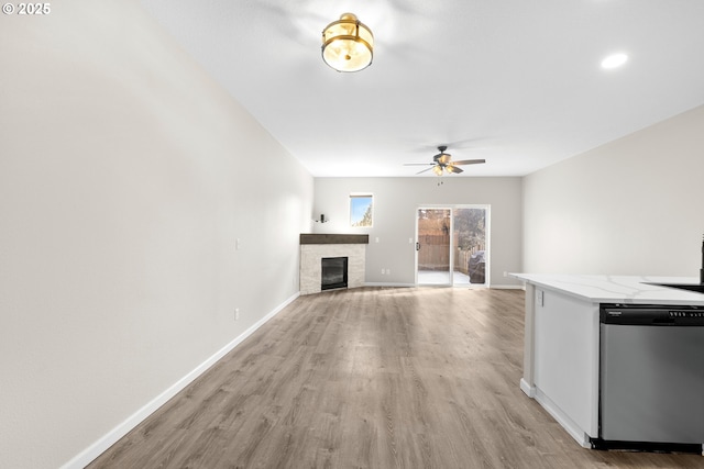 unfurnished living room featuring ceiling fan, a fireplace, light wood-type flooring, and baseboards