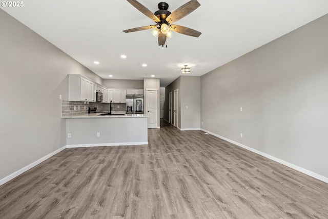 unfurnished living room featuring baseboards, light wood-style flooring, recessed lighting, ceiling fan, and a sink