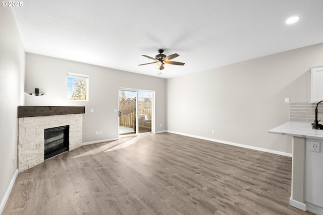 unfurnished living room featuring ceiling fan, a fireplace, baseboards, and wood finished floors