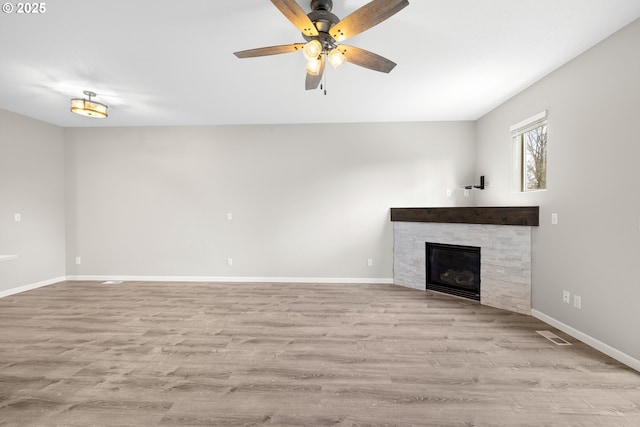 unfurnished living room featuring a glass covered fireplace, wood finished floors, baseboards, and a ceiling fan