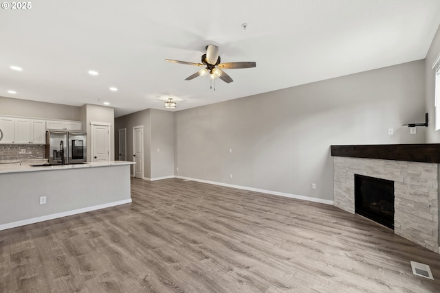 unfurnished living room with visible vents, baseboards, a stone fireplace, light wood-style floors, and a ceiling fan