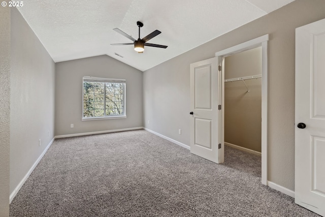 unfurnished bedroom featuring a textured ceiling, carpet flooring, baseboards, a spacious closet, and vaulted ceiling