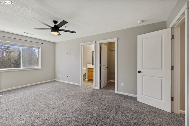 unfurnished bedroom featuring visible vents, a walk in closet, baseboards, carpet flooring, and a textured ceiling